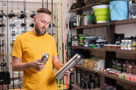 A man chooses and buys a thermal bottle in a sports store, a fisherman choosing accessories for fishingの写真素材
