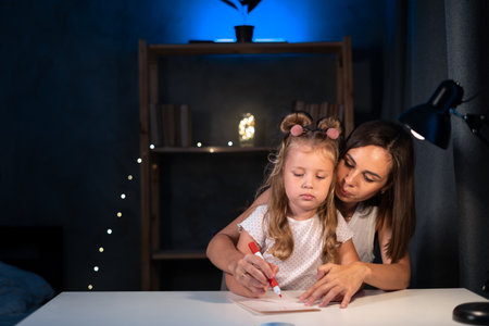 Mother teaches little preschooler to do homework by painting with color at night, image can be used for girl, study, school, mother, teacher, child, student and educationの写真素材