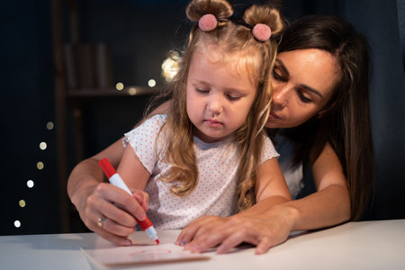 Portrait of mother and daughter drawing at home at night. Woman help child to draw. Girl from elementary class, back to school.の写真素材