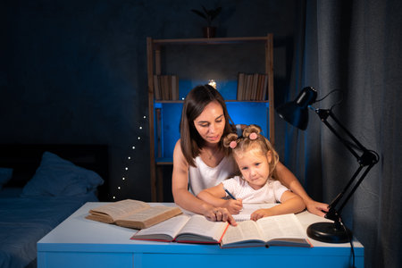 Mother and child daughter doing homework writing and reading at home in the evening.の写真素材