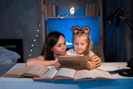 mom helps child daughter do homework at home using digital tablet. Child studying late at night. Children, family, educationの写真素材