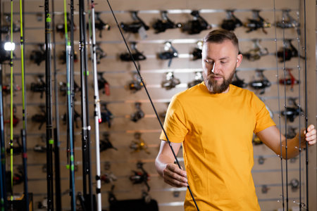 Millennial man chooses fishing rod in the sports shop, fishing storeの写真素材