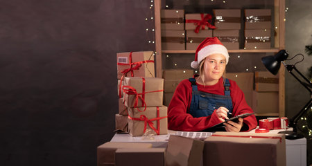 Young woman entrepreneur, small business owner in santa claus costume tired working at night in home office, preparing delivery box. christmas sale. SME concept.の写真素材