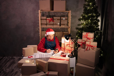 A woman salesman in a Santa Claus hat takes an order by cell phone while sitting in an office with...