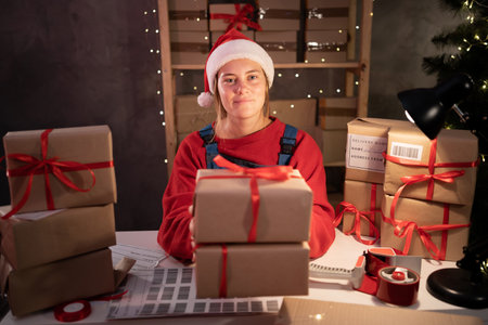 Happy girl Santa Claus packing present box wrapping gift preparing post shipping delivery parcel on table in workshop at night. Merry Christmas shipping deliveryの写真素材