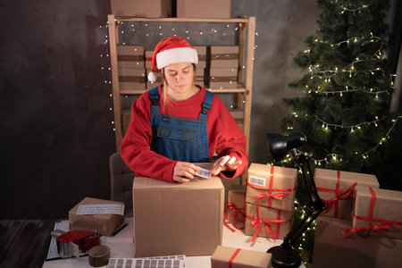 Business start up SME concept. Young female aspiring entrepreneur, small business owner, packing goods, preparing for shipment. Wearing a santa claus hat is a good income during Christmas saleの写真素材