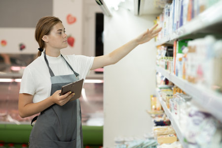 female staff standing in front of the supermarket shelf with milk using tablet pcの写真素材