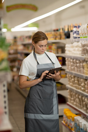 Busy female sales assistant in a grocery typing on the tablet while taking inventory.の写真素材