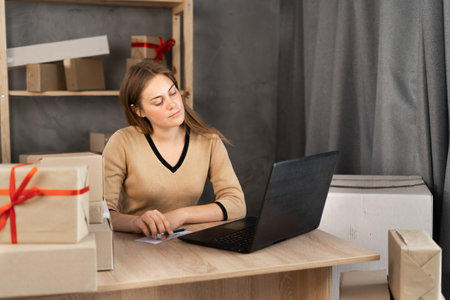 Caucasian female business owner sitting at home office using computer, online marketing packaging box delivery, SME e-commerce telemarketingの写真素材