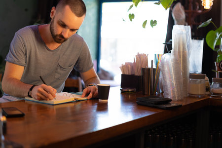 Young bar owner standing at bar counter thinking writing receipt in notebook concentrated. Job concept.の写真素材