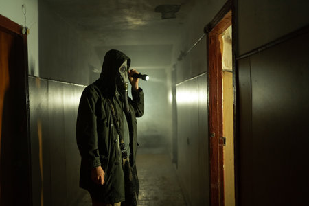 Man in respirator gas mask with flashlight inside of abandoned building in dark. Cyberpunk postapocalypse fantasy horror scene, or air pollutionの写真素材
