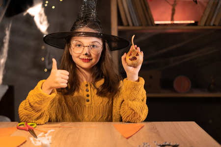 Little witch with a pumpkin in her hands at the table in the evening. Halloween Witchの写真素材