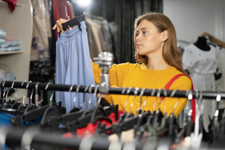 happy young woman with shopping bag choosing clothes in mall or clothing store. sale, fashion, consumerism and peopleの写真素材