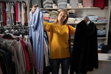 happy young woman choosing between two sweatshirts in mall or clothing store. sale, clothing, shopping, fashion and peopleの写真素材