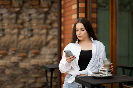 Attractive brunette woman in a street cafe reading a text message from her phone.の写真素材