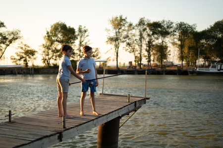 boys is fishing at sunset on the lake jetty with a fishing rod. Summer leisureの写真素材