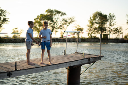 boys is fishing at sunset on the lake jetty with a fishing rod. Summer leisureの写真素材