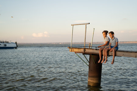 Two boys fishing with a fishing rod on a lake at sunset. Childrens summer vacationの写真素材
