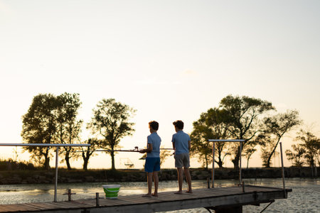 children with fishing rods stand on a wooden pier and fish at the lake. Fishingの写真素材