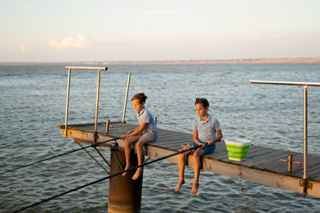 Two boys fishing at sunset on the lake, river water backgroundの写真素材