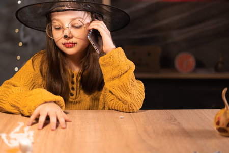 Closeup portrait, young child girl talking on cell, smart phone, indoors Halloween decor background. human emotions, facial expressions, life perception, communicationの写真素材