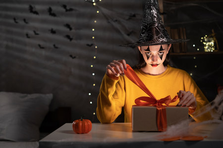 woman witch holding a gift box in her hand and untie a bow on Halloween sitting at night at home. Halloween saleの写真素材