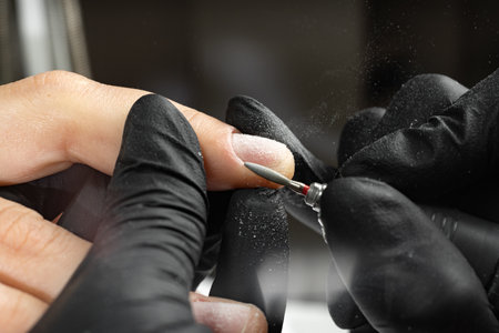 Closeup of master hands in black gloves applying an electric nail file drill to remove cuticles in the beauty salon. Perfect nails manicure process. Hardware manicureの写真素材