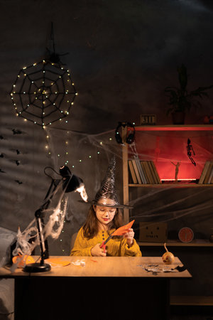 The child girl creates a hand-crafted pumpkin from paper at darkness room. a party of Halloween. Craft for kids. Pumpkin made of paper.の写真素材