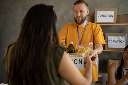 Cardboard box with food donations. Young people volunteering to sort donations for charity food drive. volunteering in food bankの写真素材