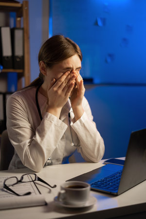 Tired woman doctor with vision problem sit at table use laptop working at night. copy spaceの写真素材