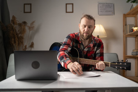 Young composer man composing song using guitar and laptop at home writing notes. copy spaceの写真素材