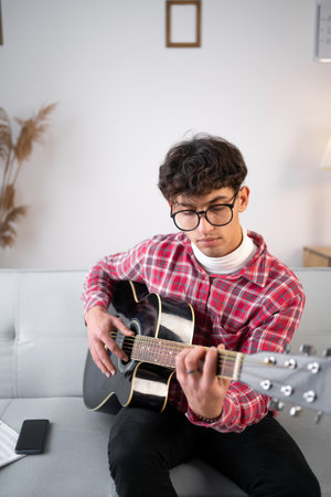 Portrait of young arabic man playing the acoustic guitar at home. copy spaceの写真素材