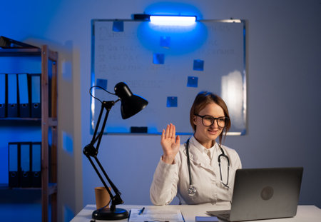 Attractive female doctor make online video call consult patient on laptop working at hospital office at night. Therapist videoconferencing to webcam. telemedicine concept. copy spaceの写真素材