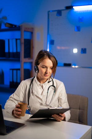 Medicine doctor working at night with clipboard and modern laptop computer, holding coffee cup in the hand. copy spaceの写真素材