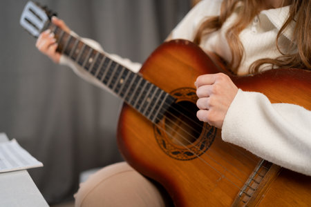 Woman playing acoustic guitar at home, female hands with guitar, close up.の写真素材