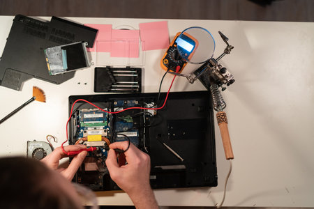 Radioman testing electric current in circuit board of disassembled laptop using multimeter. man measures voltage with ammeter on motherboard, top view. copy spaceの写真素材