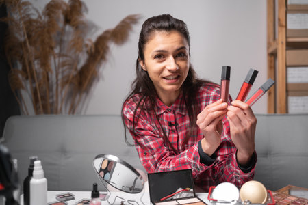 Influencer hispanic girl live streaming cosmetics product review in home studio. Vlogger female comparing lipsticks. Professional beauty make up artist vlogger or blogger recording makeup tutorialの写真素材