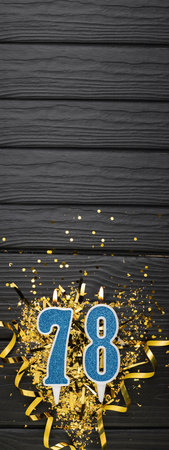 Number 78 blue celebration candle and gold confetti on dark wooden background. 78th birthday card. Anniversary and birthday concept. vertical banner. copy spaceの写真素材