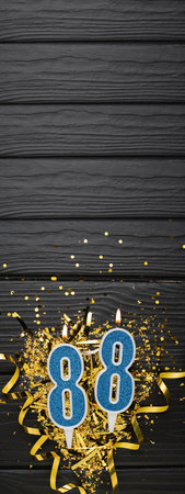 Number 88 blue celebration candle and gold confetti on dark wooden background. 88th birthday card. Anniversary and birthday concept. vertical banner. copy spaceの写真素材