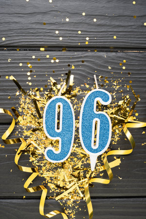 Number 96 blue celebration candle and gold confetti on dark wooden background. 96th birthday card. Anniversary and birthday concept. vertical banner. copy spaceの写真素材