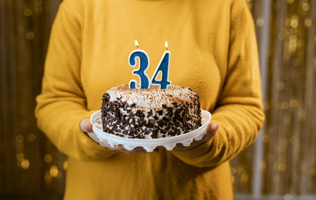 Woman holding a delicious cake with number 34 candles while celebrating birthday party. Birthday holiday party people conceptの写真素材