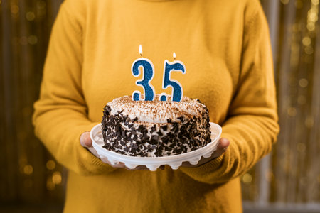 Woman holding a delicious cake with number 35 candles while celebrating birthday party. Birthday holiday party people concept.の写真素材