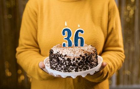 Woman holding a delicious cake with number 36 candles while celebrating birthday party. Birthday holiday party people concept.の写真素材