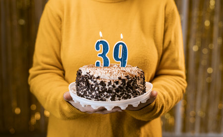 Woman holding a delicious cake with number 39 candles while celebrating birthday party. Birthday holiday party people concept.の写真素材