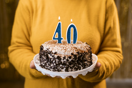 Woman holding a delicious cake with number 40 candles while celebrating birthday party. Birthday holiday party people concept.の写真素材