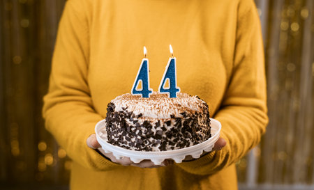 Woman holding a delicious cake with number 44 candles while celebrating birthday party. Birthday holiday party people concept.の写真素材