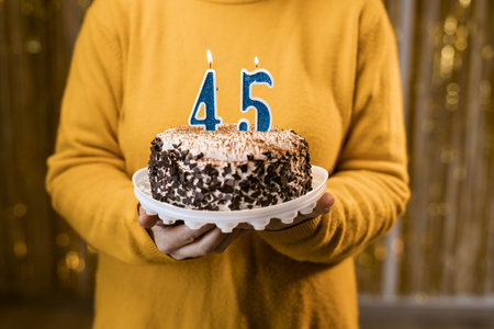 Woman holding a delicious cake with number 45 candles while celebrating birthday party. Birthday holiday party people concept.の写真素材