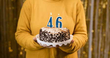 Woman holding a delicious cake with number 46 candles while celebrating birthday party. Birthday holiday party people concept.の写真素材