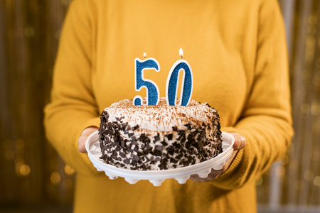Woman holding a festive cake with number 50 candles while celebrating birthday party. Birthday holiday party people concept.の写真素材