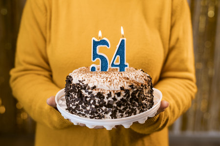 Woman holding a festive cake with number 54 candles while celebrating birthday party. Birthday holiday party people concept.の写真素材